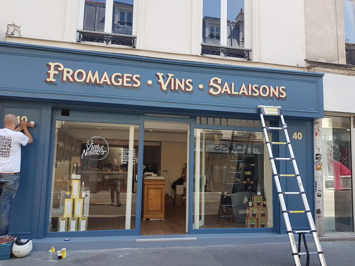 La pose de l'enseigne dorée Fromages Vins Salaisons sur la devanture des Établissements Moots